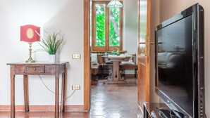 A room with a wooden cabinet, a table with a lamp, a television, and a window with a view of trees. - Wonderful private villa for 8 people with WIFI, A/C, TV, patio and panoramic view (Carassai)