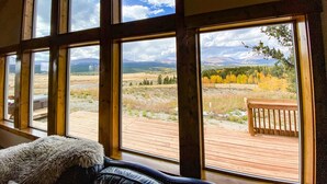 Habitación con ventanas amplias que ofrecen vista a una terraza de madera y un paisaje montañoso.