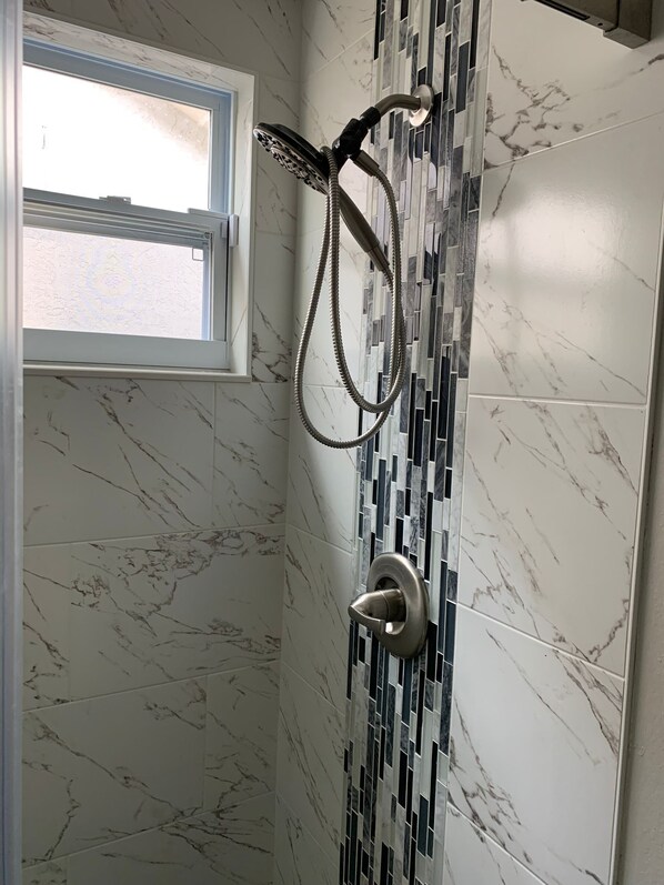 Un baño con ducha, ventana y pared con azulejos de diseño marmolado.