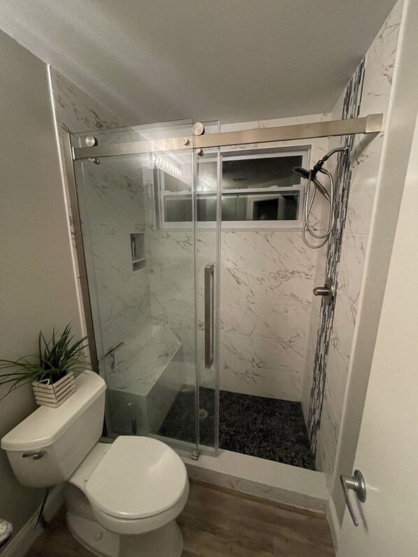Un baño moderno con ducha envuelta en vidrio, inodoro y salpicadero de mármol.