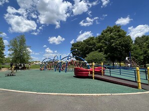 Un parque infantil con diversas estructuras de juego, una zona vallada y árboles al fondo.