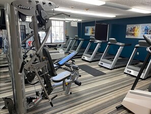 Un gimnasio con cintas de correr, máquinas de pesas y un espejo grande.