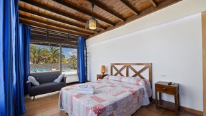 Quarto com cama, mesa de cabeceira, luminária e vista para uma piscina e palmeiras.