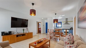 Uma sala de estar moderna com televisão de tela plana, móveis de madeira e um espaço de refeições com cadeiras e mesa.