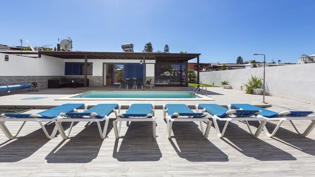 Uma área de piscina no terraço, com espreguiçadeiras azuis e um espaço de estar coberto.