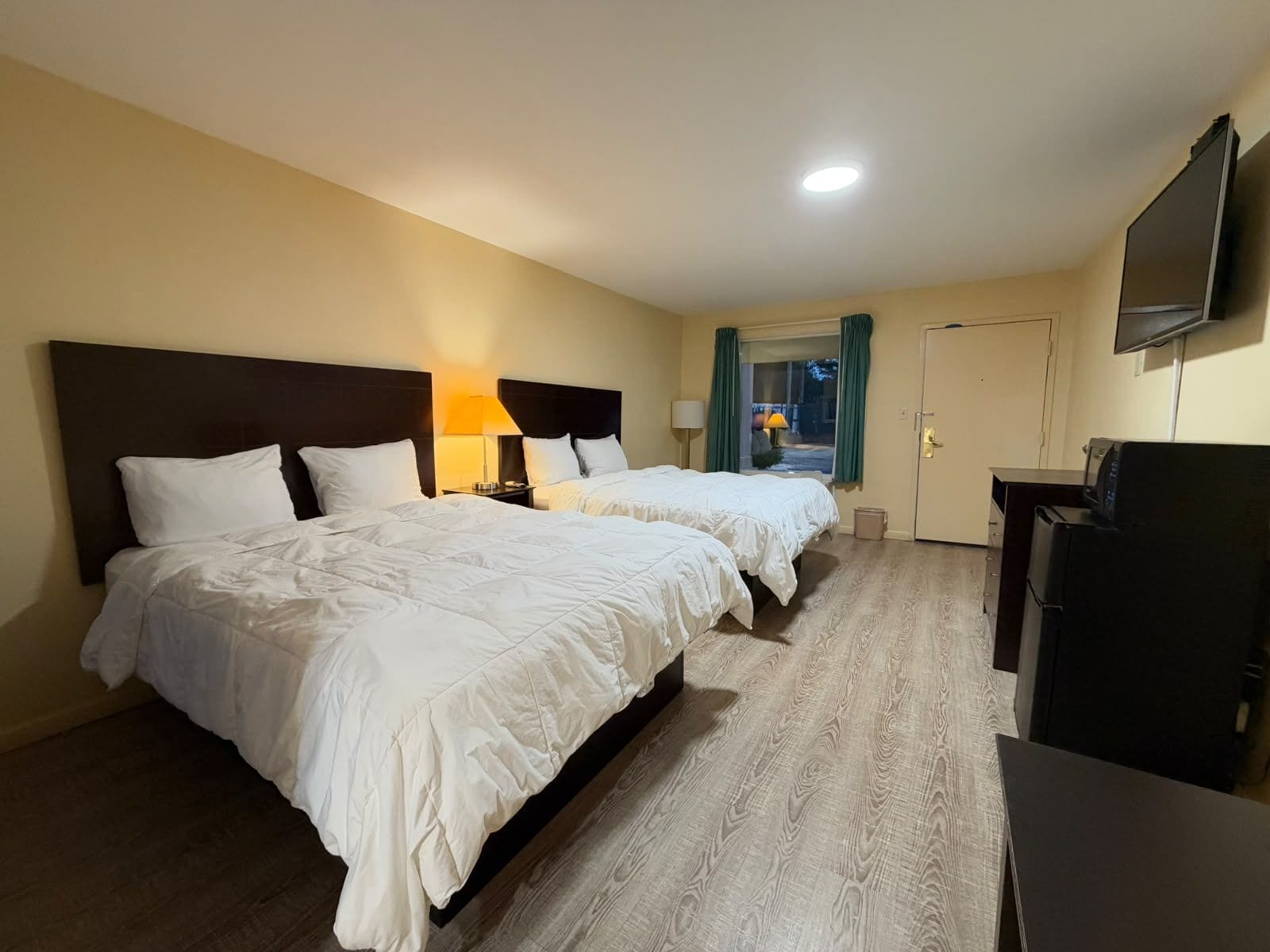 Habitación de hotel con dos camas, un escritorio, un televisor y una ventana con cortinas.