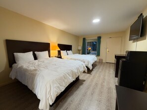 Habitación de hotel con dos camas, un escritorio, un televisor y una ventana con cortinas.