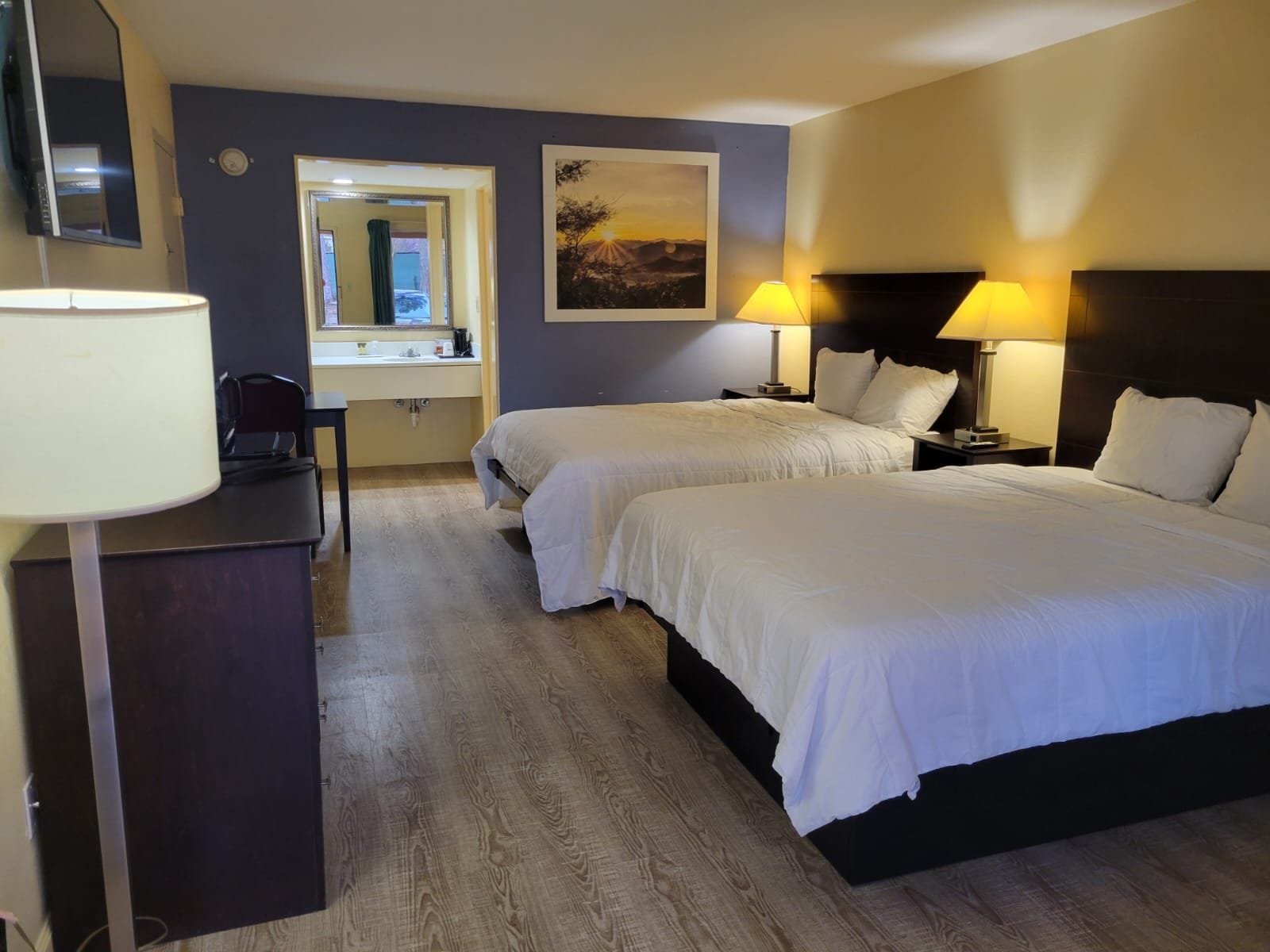 Ein Hotelzimmer mit zwei Betten, einem Schreibtisch mit Stuhl, einem Spiegel und einem Bild an der Wand.