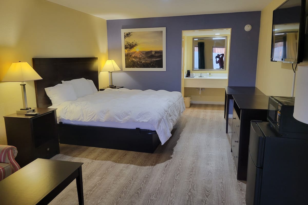 A hotel room with a bed, bedside lamps, a painting, a mirror, a TV, and a desk.