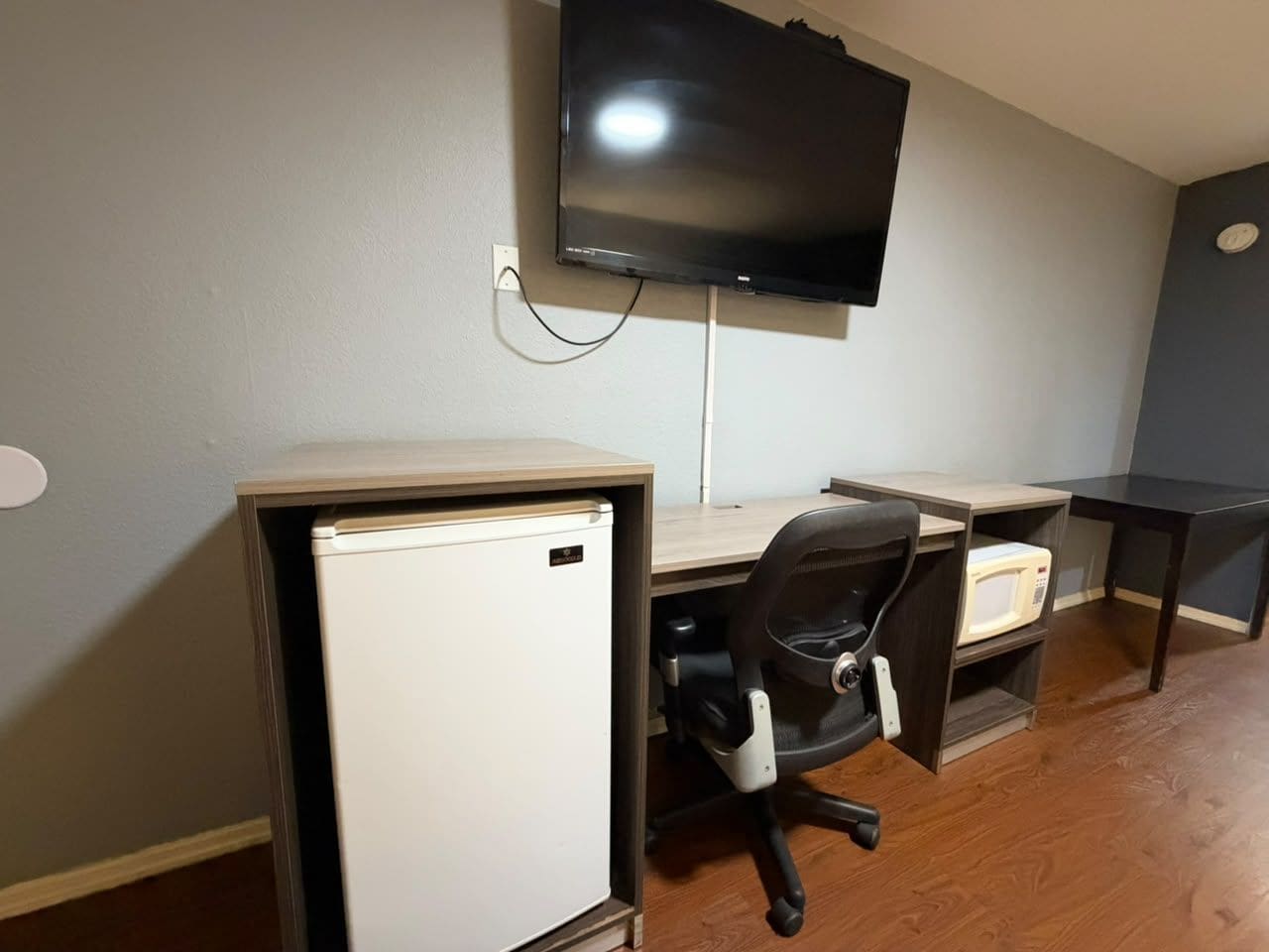 Un espacio de trabajo compacto con escritorio, silla y un refrigerador pequeño.