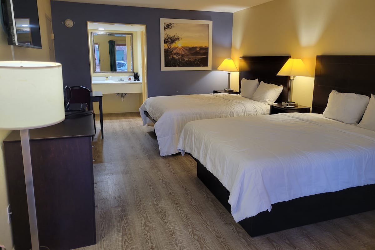 A hotel room with two beds, a desk, a chair, a mirror, and a painting on the wall.