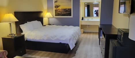 Habitación de hotel con cama, lámparas de noche, un cuadro, espejo, televisor y escritorio.