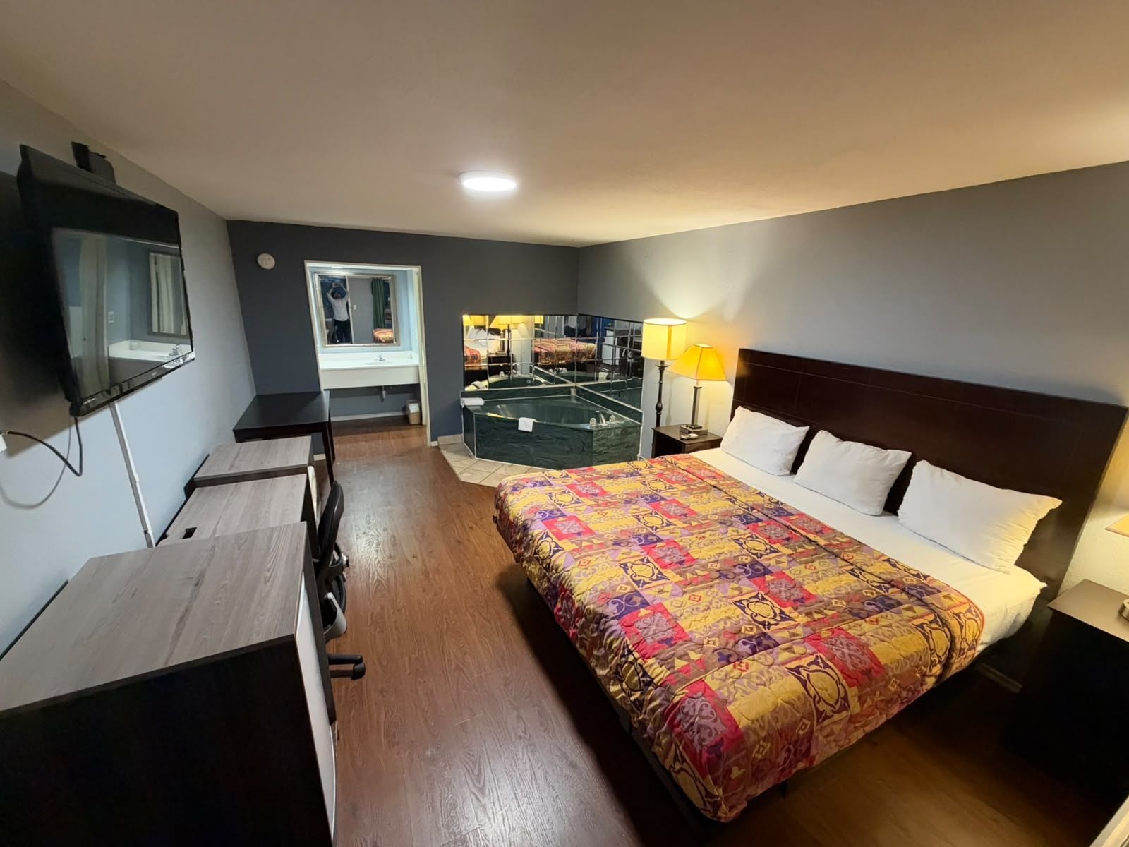 Habitación de hotel con cama, mesitas de noche, escritorio, espejo y baño visible a través de una puerta abierta.