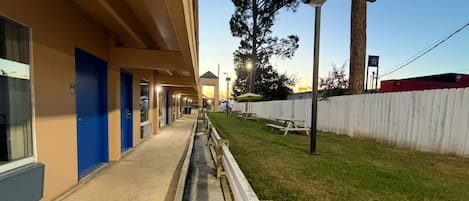 A building with a long, straight corridor leading to a grassy area with picnic tables.