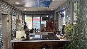 Zona de recepción con mostrador, estatua de Buda, reloj y ventana con persianas.