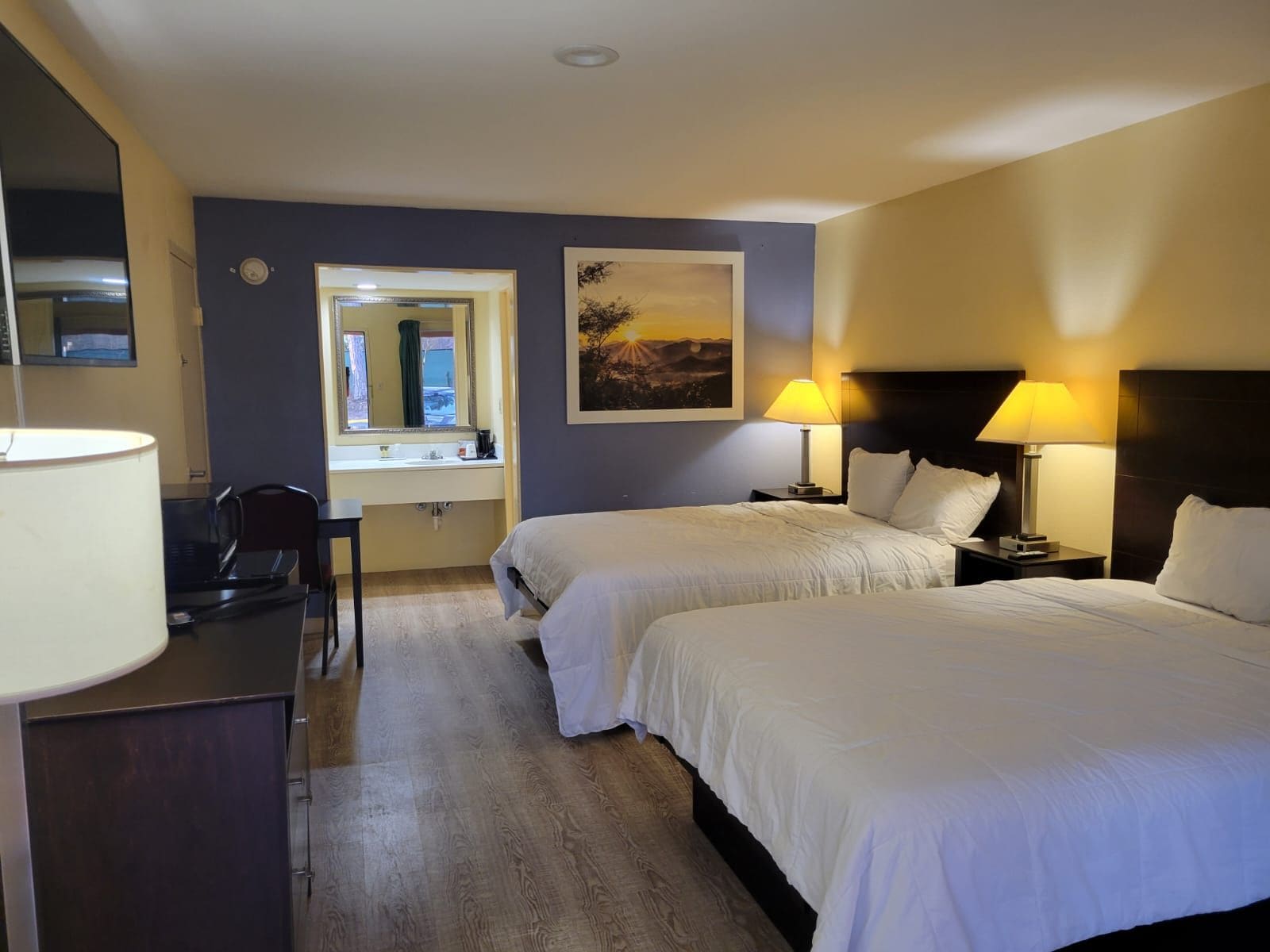 Une chambre d’hôtel avec deux lits, un bureau, une chaise, un miroir et un tableau au mur.