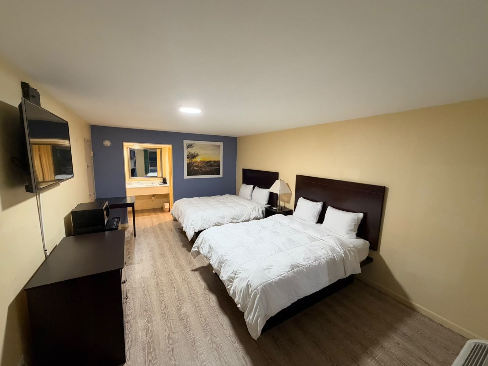 A hotel room with two beds, a desk, a TV, and a painting on the wall.
