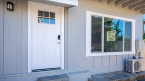 A house with a white front door, a large window, and a small air conditioning unit on the porch.