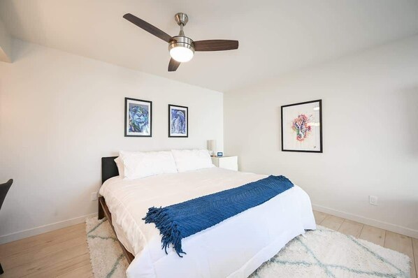 Une chambre à coucher avec un lit, un ventilateur de plafond et trois œuvres d’art encadrées accrochées au mur.