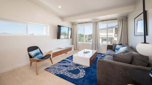 A modern living room with a sofa, a coffee table, a TV, and a large window with curtains.