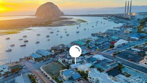 An aerial view of a coastal town with a marina, buildings, and a prominent mountain in the background.