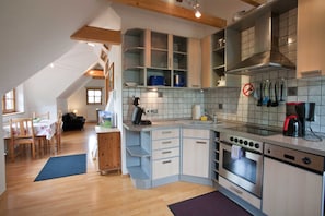 A kitchen with a stove, oven, and sink, wooden cabinets, and a dining area with a table and chairs.