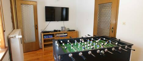 A room with a foosball table, a television, and a refrigerator.