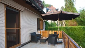 Une terrasse extérieure aménagée avec des meubles en osier, une clôture en bois et un grand parasol.