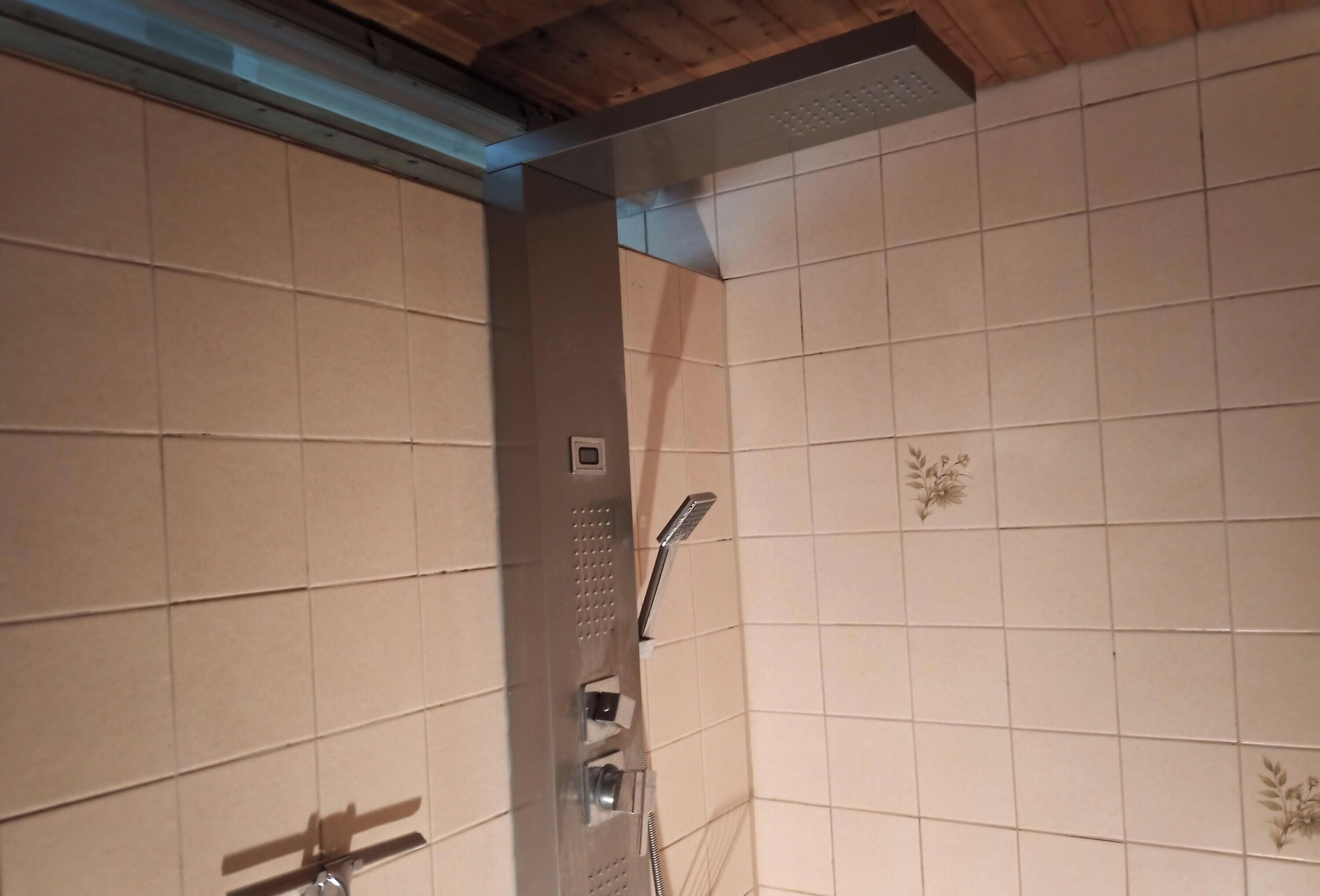 Ein gefliester Duschbereich mit Duschkopf, Bedienfeld und Holzboden.