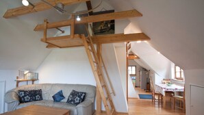 Une pièce de style « loft », avec un escalier en bois, un canapé, une table basse et un coin repas.