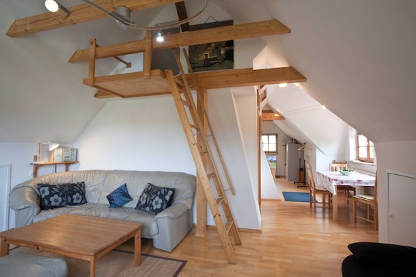 A loft-style room with a wooden staircase, a sofa, a coffee table, and a dining area.
