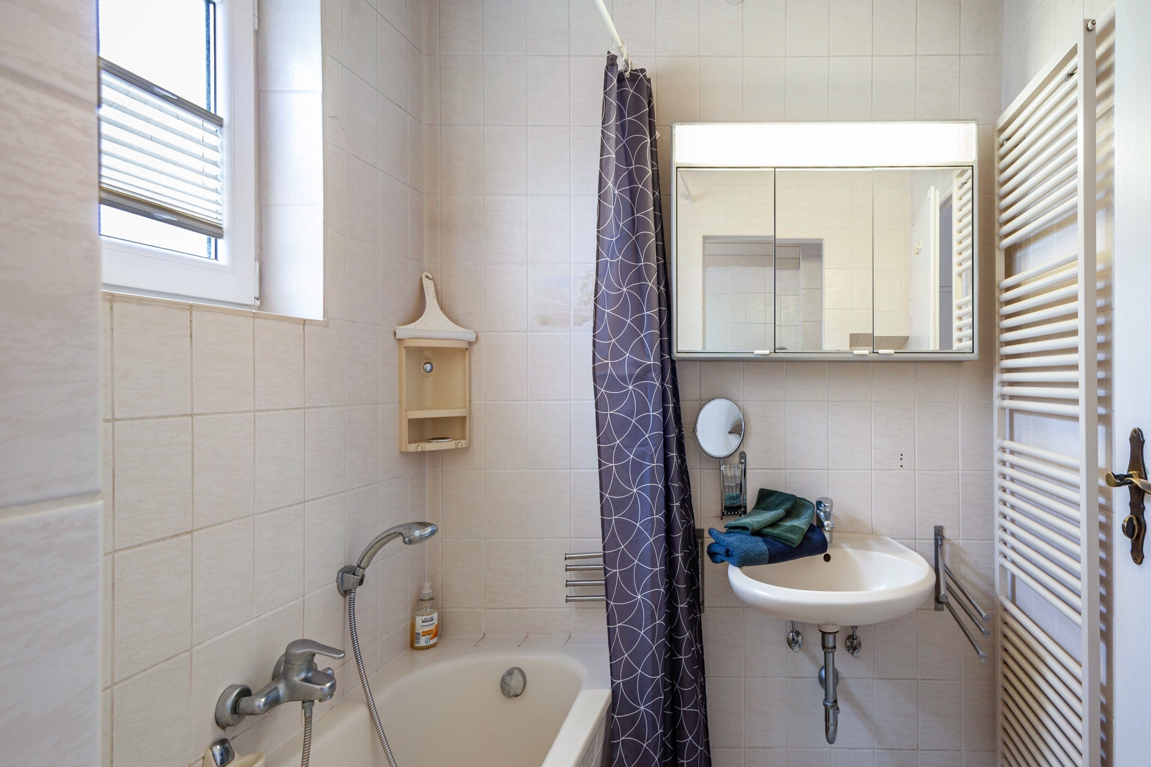 A bathroom with a bathtub, a sink, a mirror, and a window with blinds.
