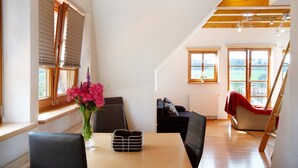 A dining area with a table, chairs, a vase with flowers, and a view of the outdoors through large windows.