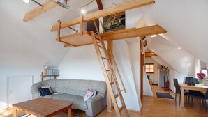 A loft-style room with a wooden ceiling, a gray sofa, a wooden table, and a ladder.