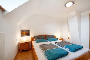 A bedroom with a sloped ceiling, a wooden bed frame, a bedside table, a wall-mounted lamp, and a painting on the wall. - 'Ferienhaus im Allgäu - Small Apartment' with Whirlpool & Wi-Fi (Weiler im Allgäu)