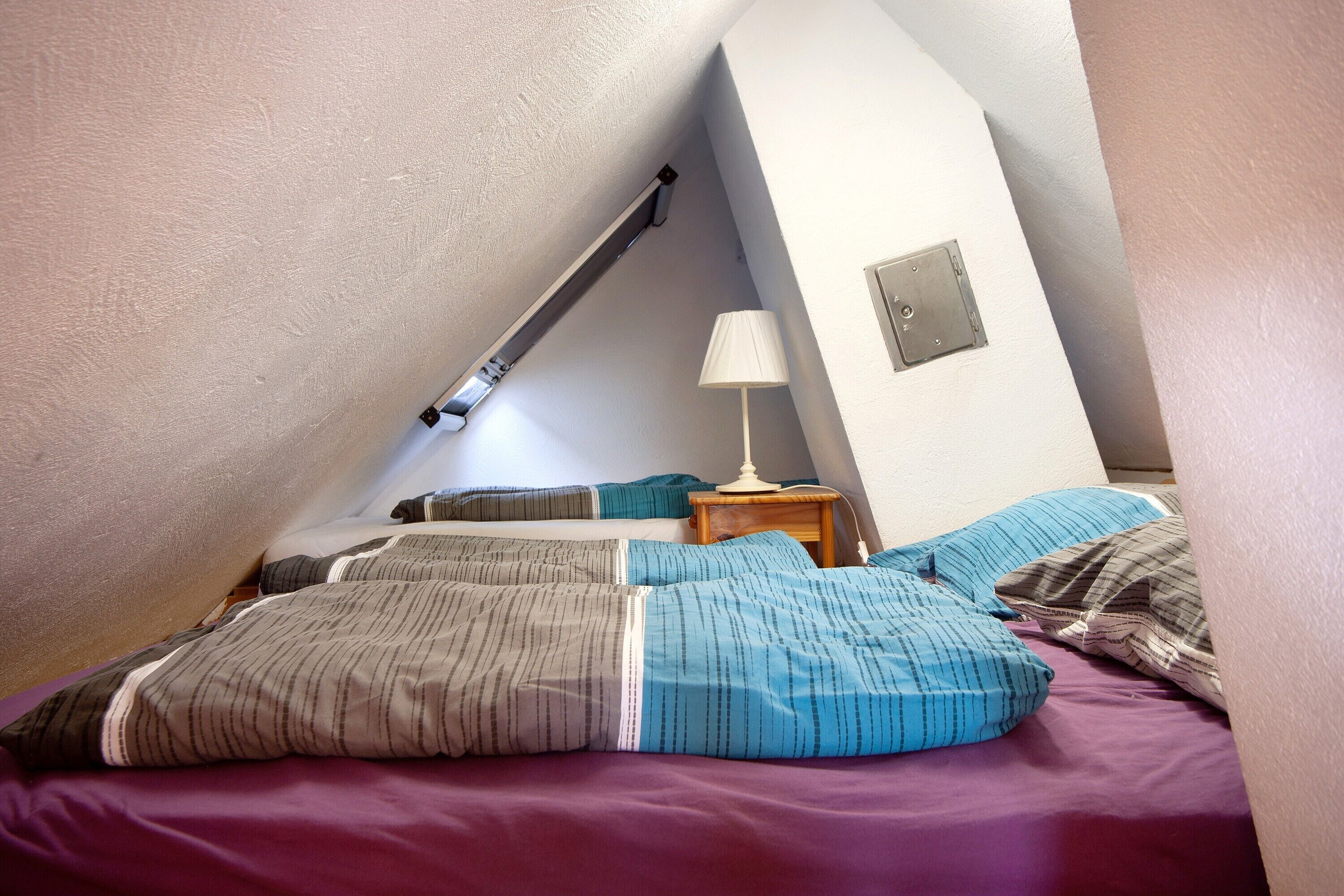 A bedroom with a sloped ceiling, a bedside lamp, and a wooden nightstand.