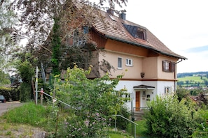 A two-story house with a sloped roof, a visible chimney, and a front door. - 'Ferienhaus im Allgäu - Small Apartment' with Whirlpool & Wi-Fi (Weiler im Allgäu)