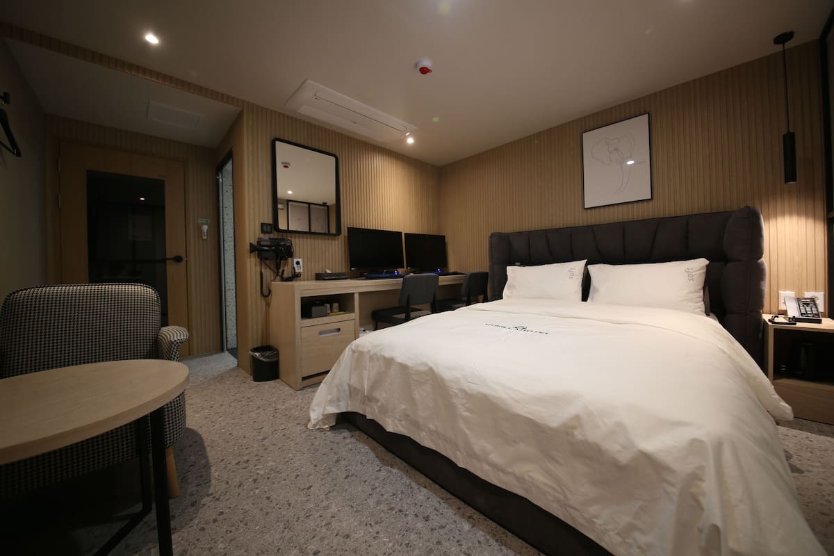 Une chambre d’hôtel avec un grand lit, un bureau doté de deux écrans, une chaise et une petite table.