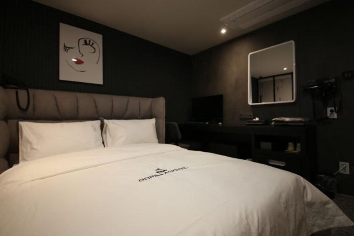 Een hotelkamer met een bed, een hoofdeinde, een bureau, een spiegel en een wand met een kunstwerk.