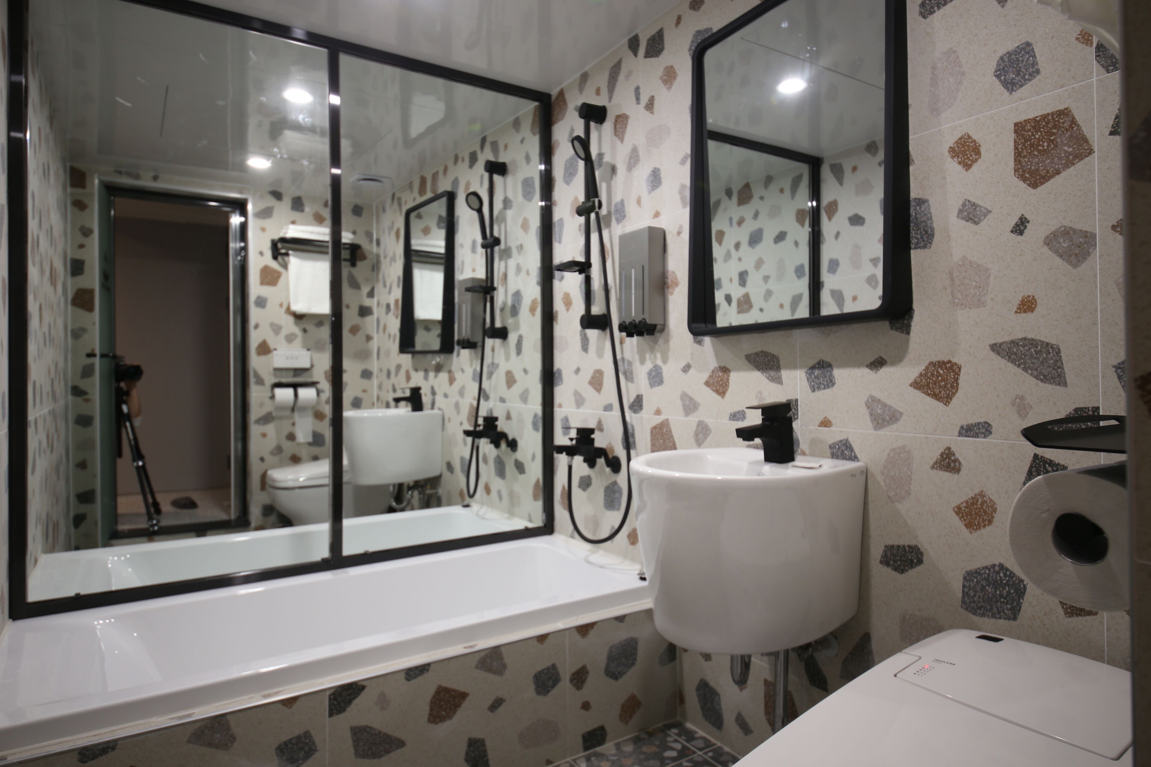 A modern bathroom with a large mirror, a bathtub, a sink, and a toilet.
