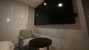 Une pièce avec une porte coulissante fermée, une table ronde noire, un fauteuil à carreaux et un téléviseur à écran plat fixé au mur.