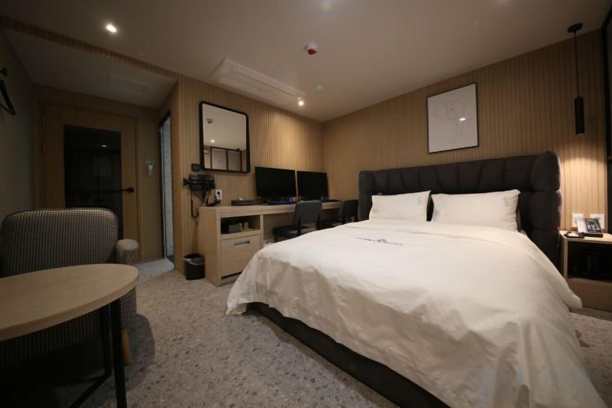 A hotel room with a bed, desk, chair, and a small table.
