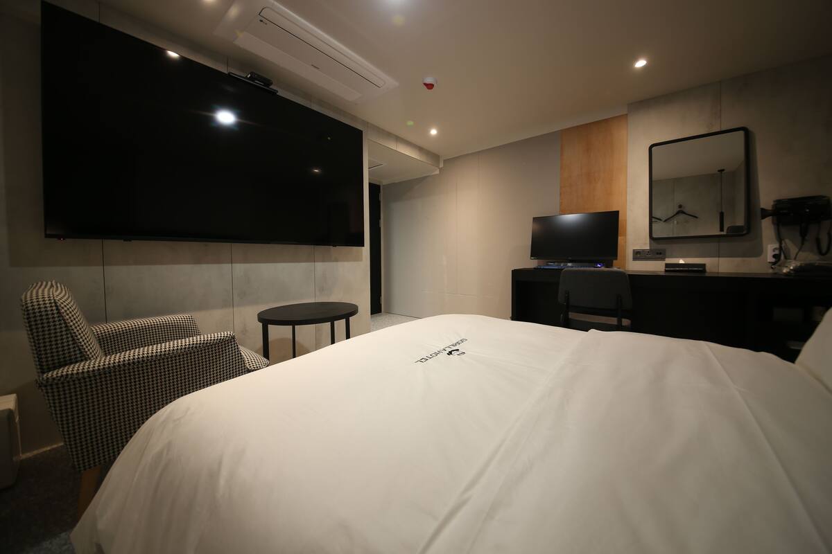 Une chambre d’hôtel avec un grand lit, un téléviseur à écran plat fixé au mur, un bureau avec une chaise et une petite table ronde.