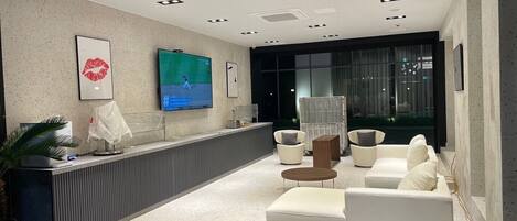 Una zona de recepción moderna con televisor de pantalla plana, asientos y una planta.