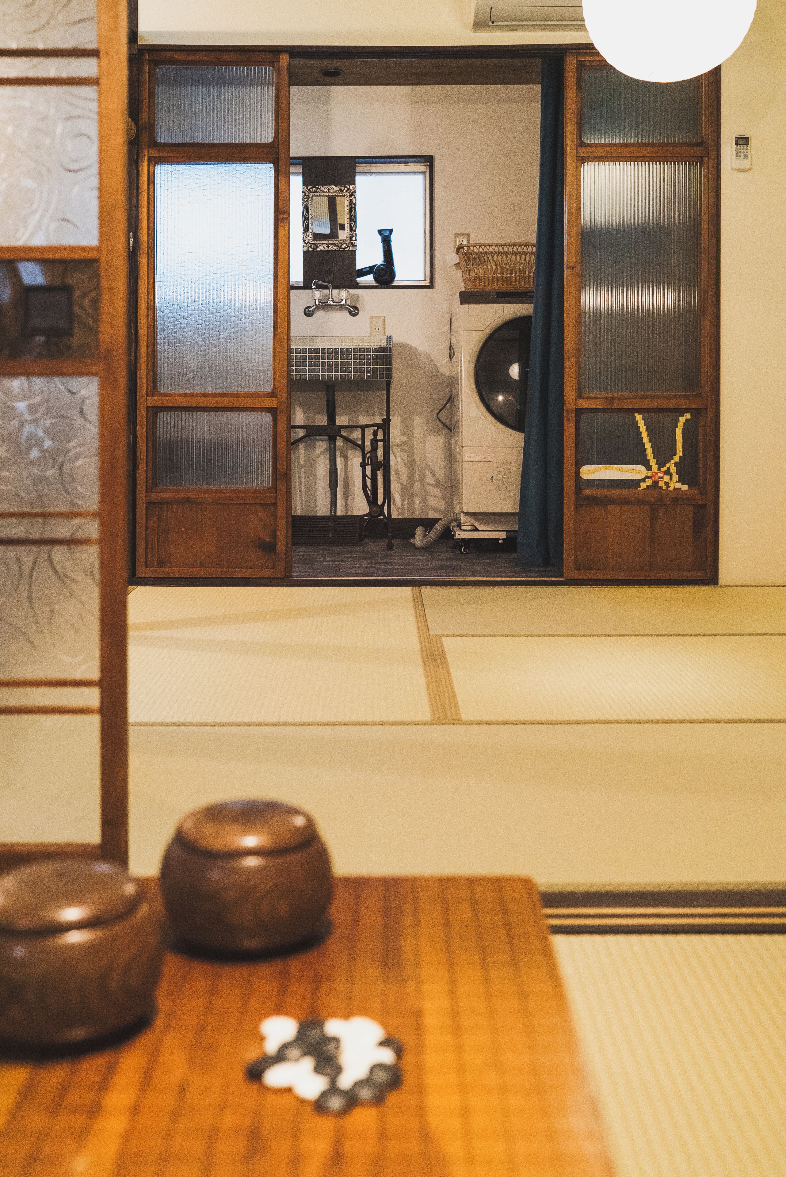 A tatami mat room with a traditional Japanese aesthetic, including a shoji screen door, a futon bed, and a low table with a tea set.