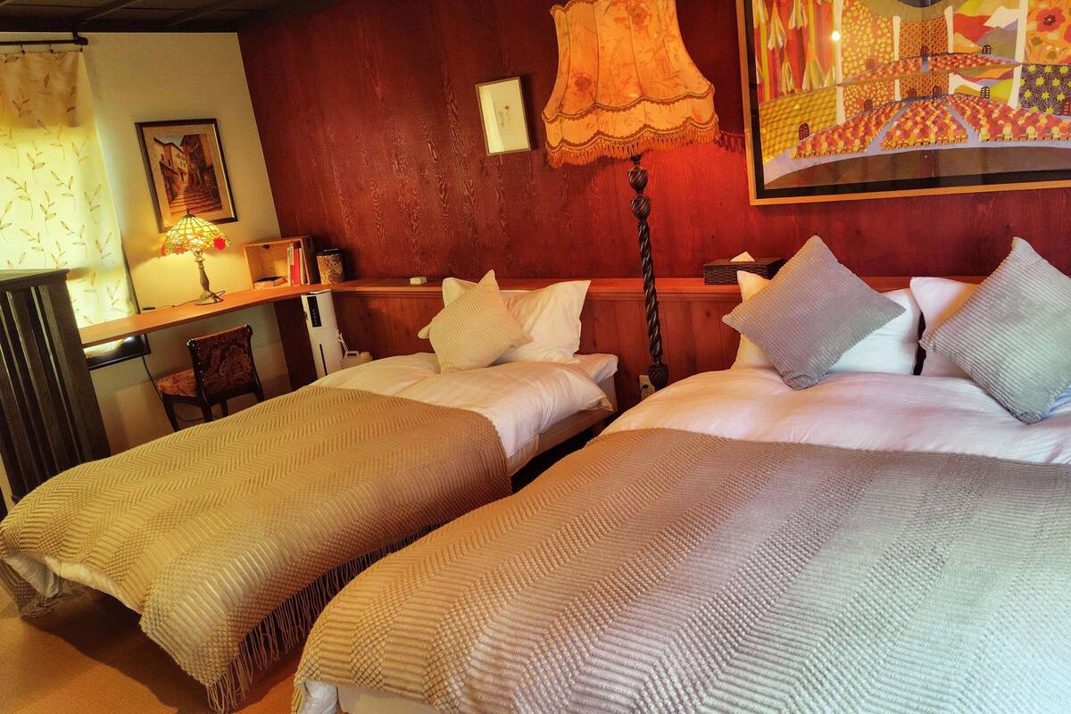 A hotel room with two beds, a desk, a chair, a lamp, and a painting on the wall.