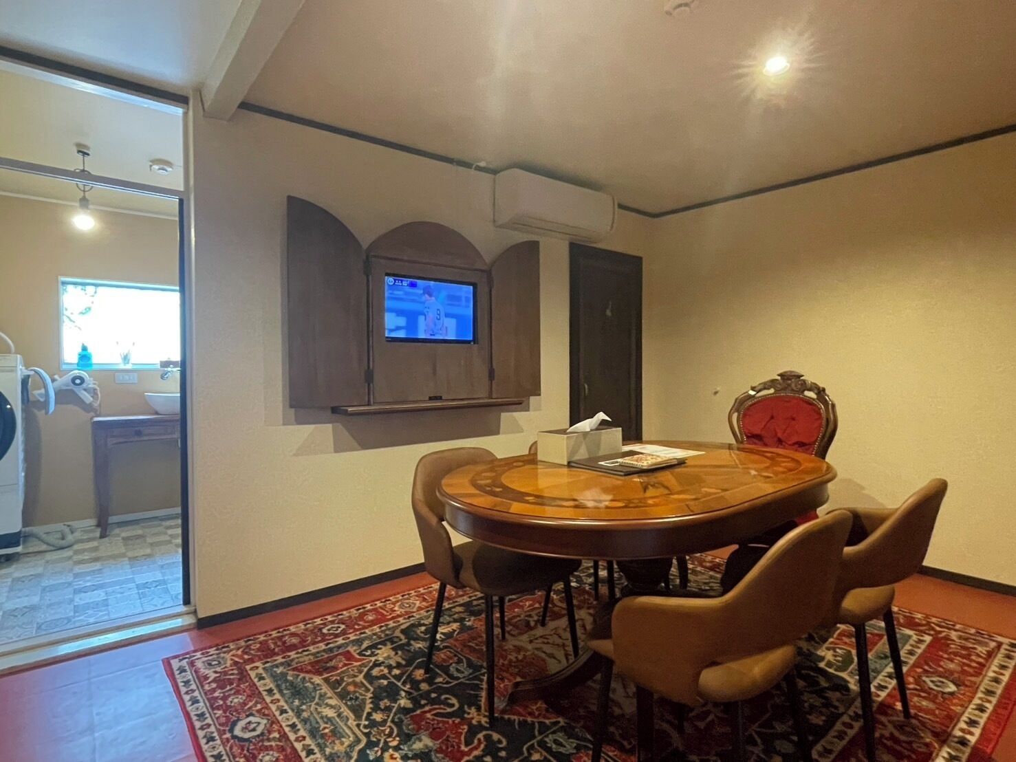 Een eetgedeelte met een ronde tafel, vier stoelen, een aan de muur bevestigde televisie en een kamerbreed tapijt.