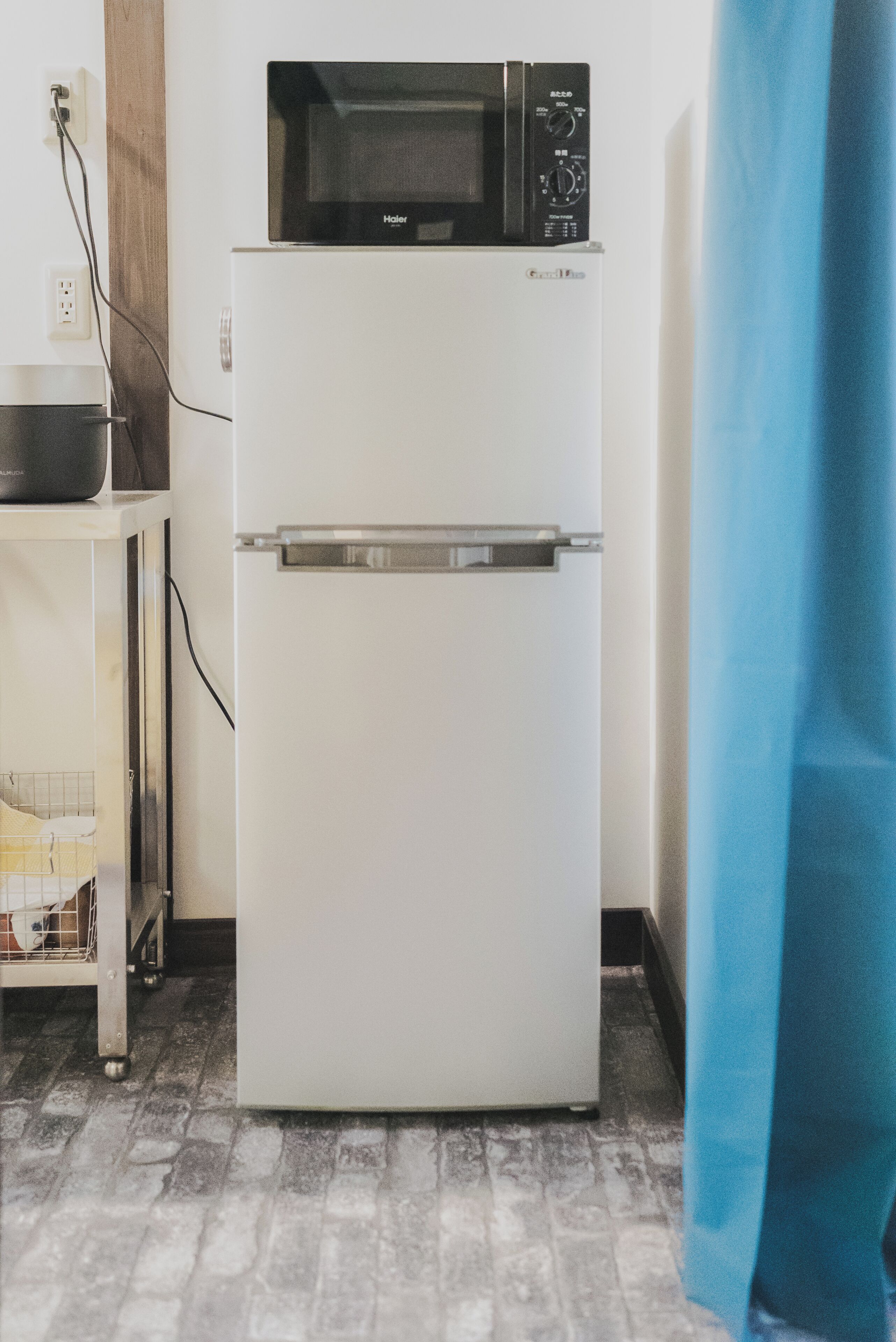 Un refrigerador compacto con un microondas encima, un enchufe y una pequeña mesa con una cesta.