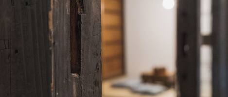 A wooden door with a visible gap, leading to a room with a bed and a wooden wall.