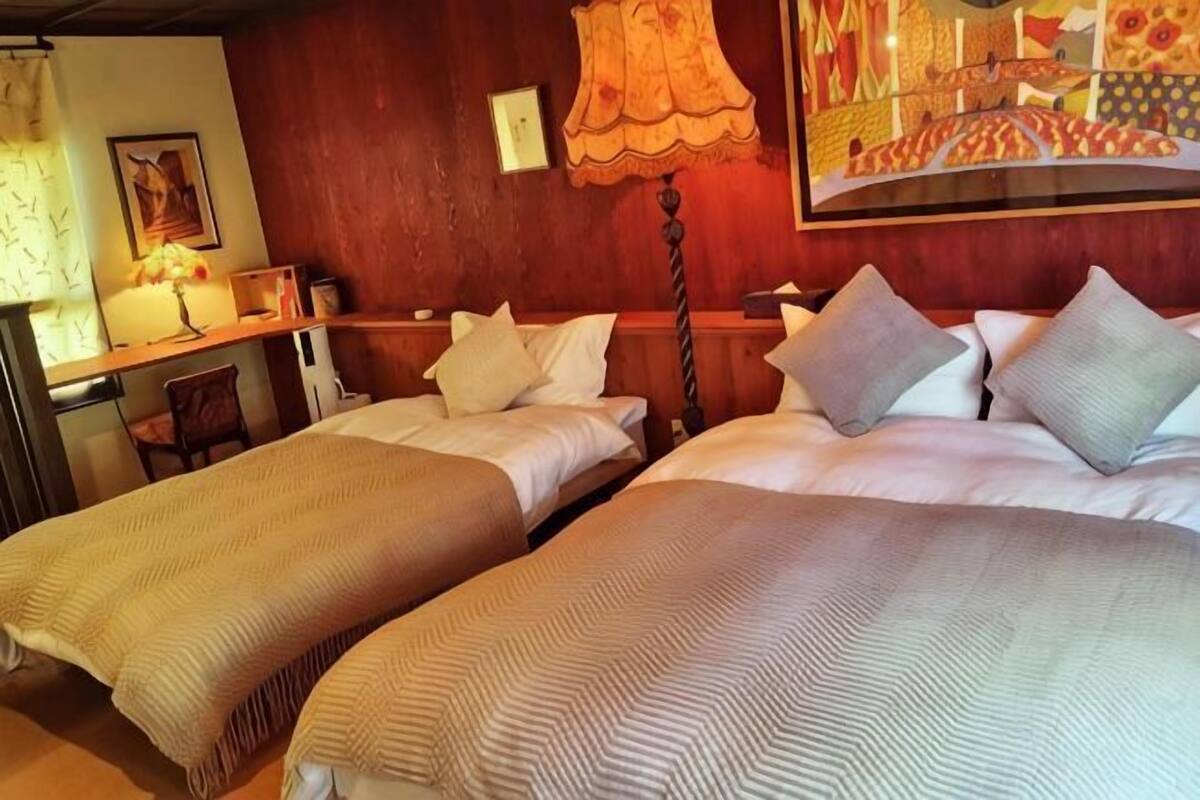 A hotel room with two beds, a desk with a lamp, and a painting on the wall.